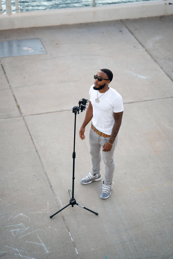 Man standing on a rooftop with a microphone stand, wearing sunglasses and a white t-shirt.